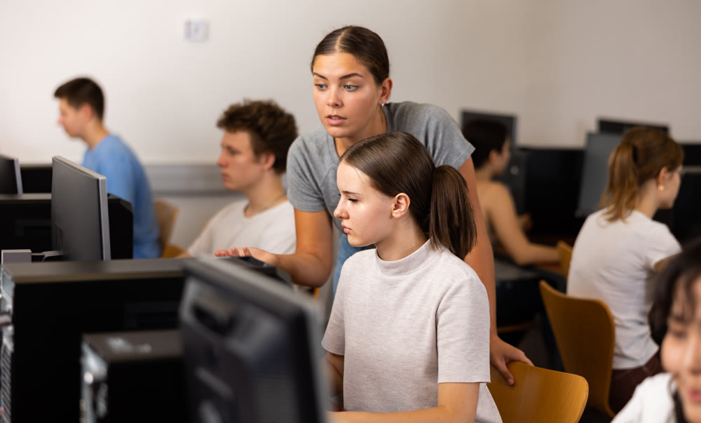 Focused female student explaining the topic to female friend while she is studying computer science on the pc in the classroom