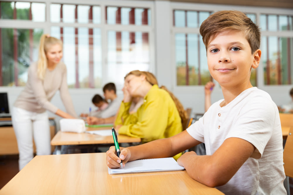 Boy listening to lecturer and writing in notebook in classroom
