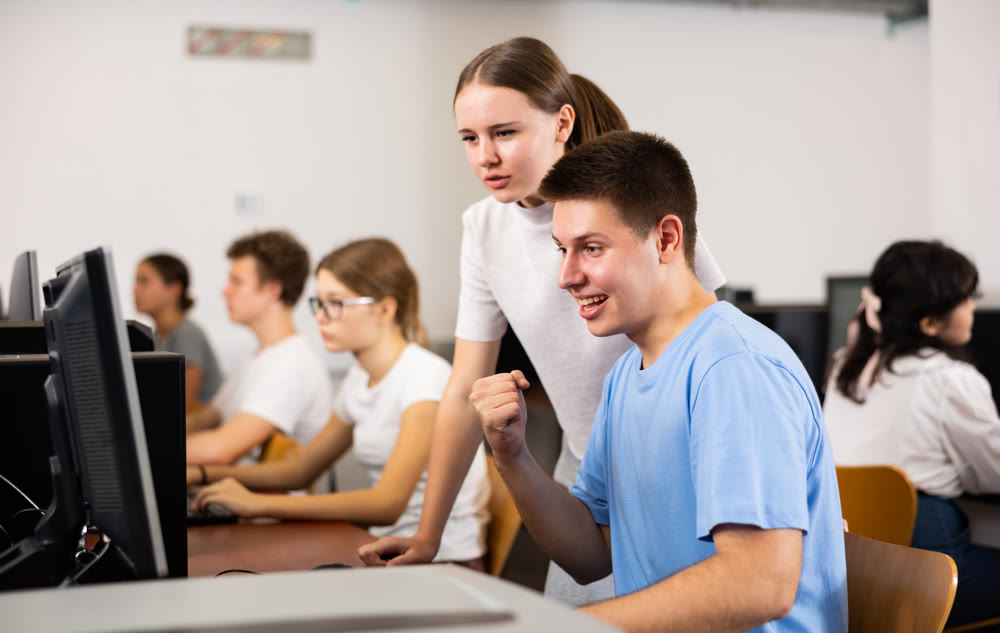 Smiling teenagers using computer during computer science lesson