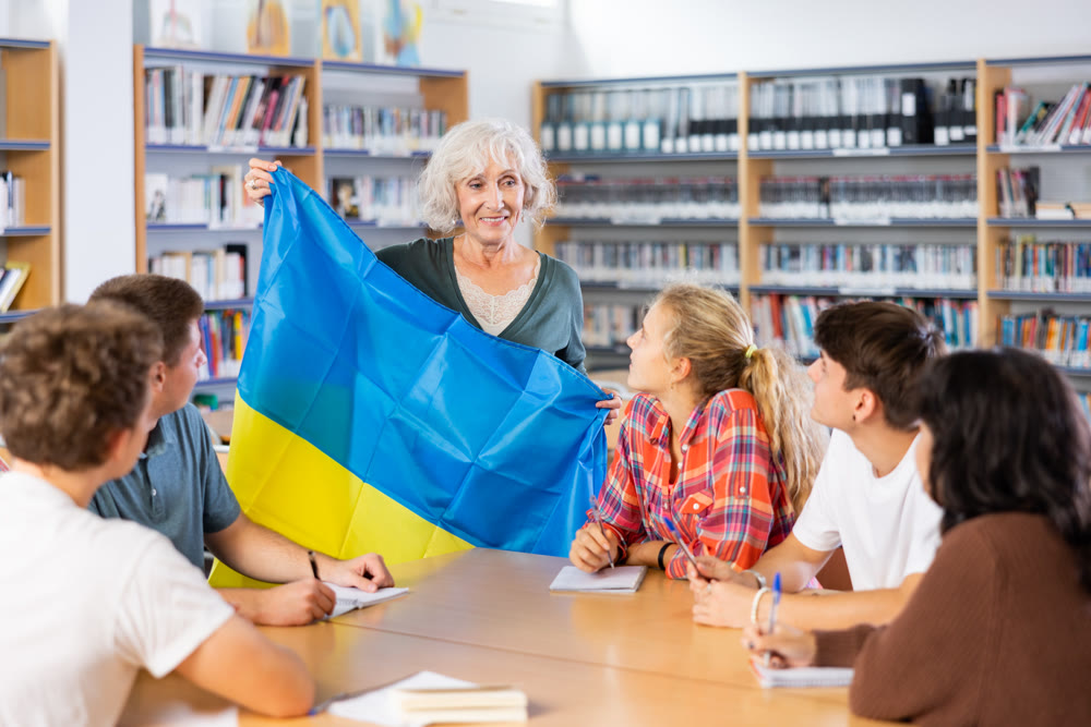 Interesting story about Ukraine while teaching high school students in school library. Teacher holds flag of Ukraine in her hands