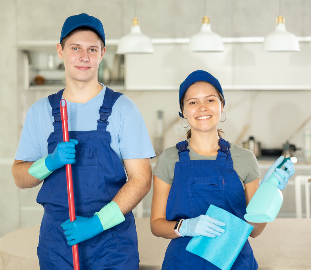 Young workers of cleaning service in blue uniform posing with cleansing tools in hands