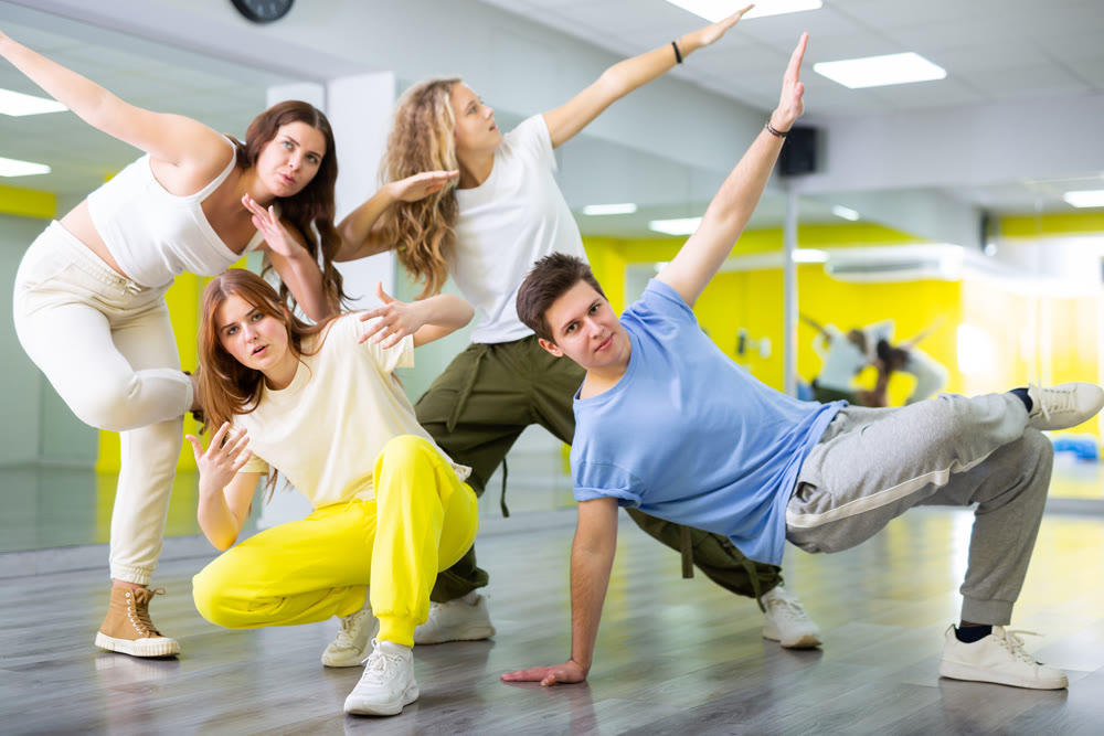 Teenage girls and a boy performing breakdance poses in dance hall