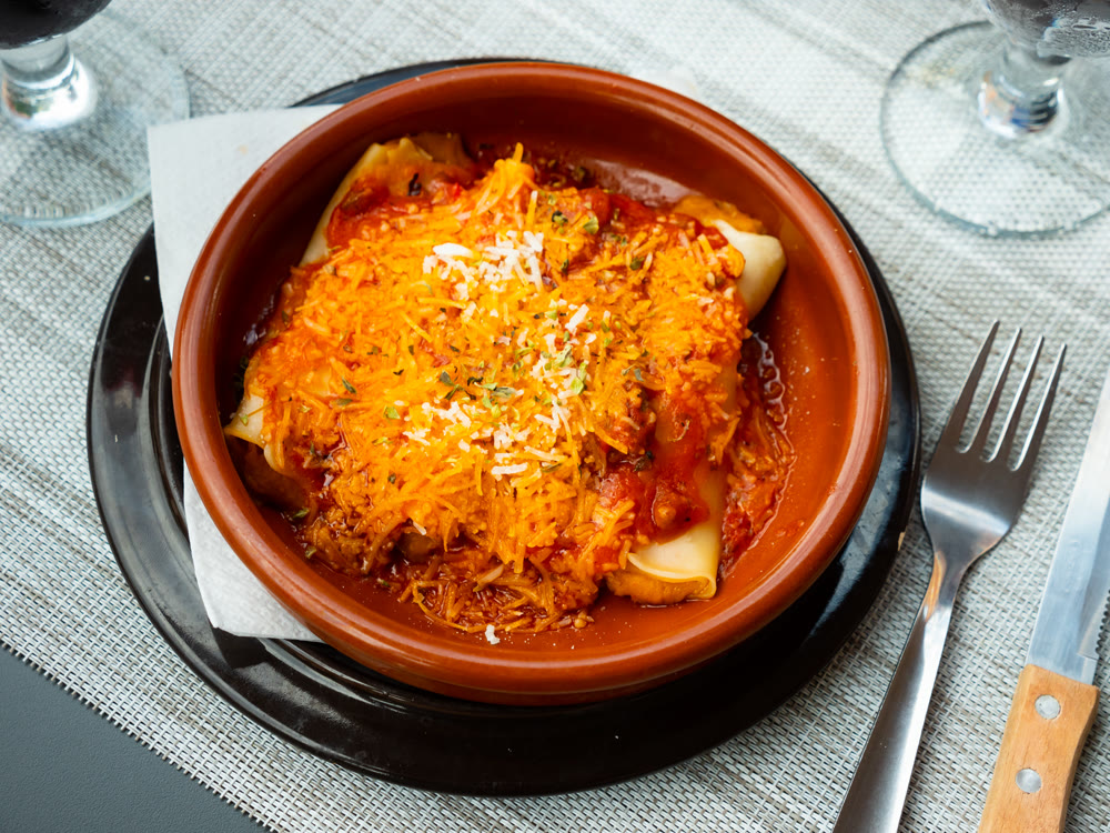 Delicious pasta cannelloni with meat and tomato sauce served in clay plate. Traditional Italian dish