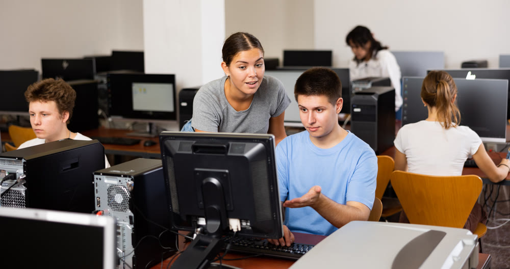 Woman teacher helps guy with learning on computer in school