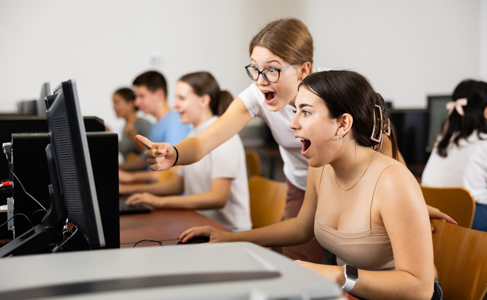 Surprised teenage girls emotionally react to solving problem in computer class