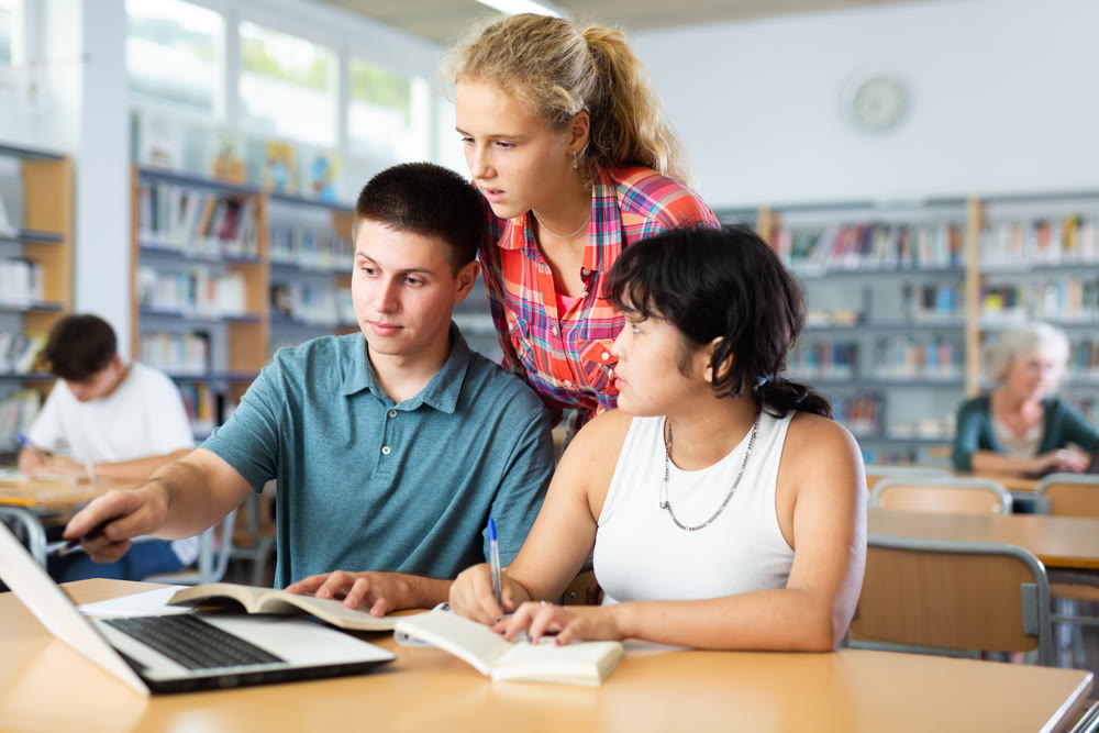 Teenagers noisily discussing something while looking at laptop screen in school library