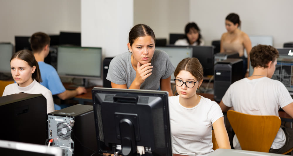 Woman teacher helps girl with learning on computer in schoolclass