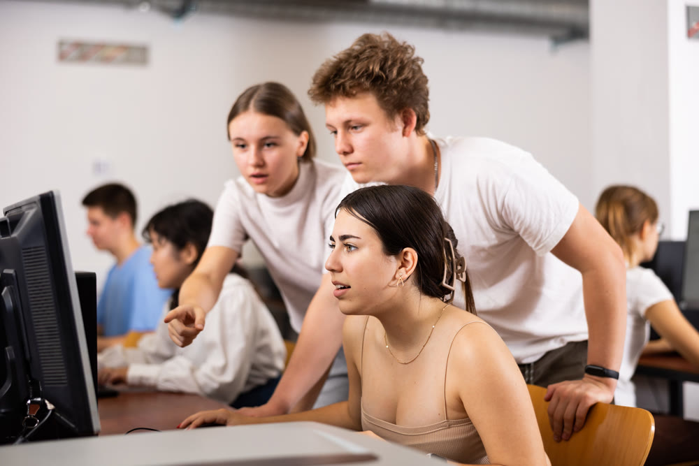 Young boy and girls student emotionally reacting while studying at computer in technology class