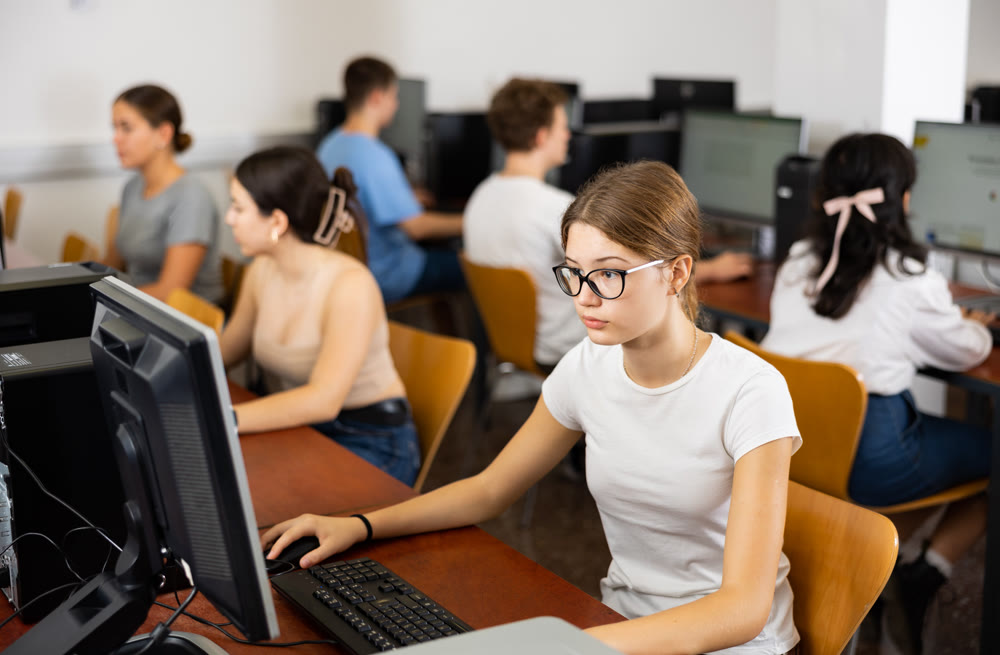 Interested young female student with glasses working on computer in library, looking for necessary information on Internet