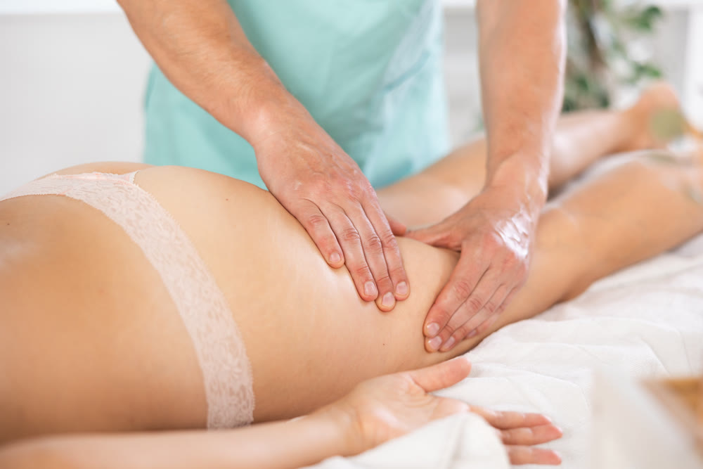 Woman covered with white towel lies and enjoys during anti-cellulite massage in hips and legs