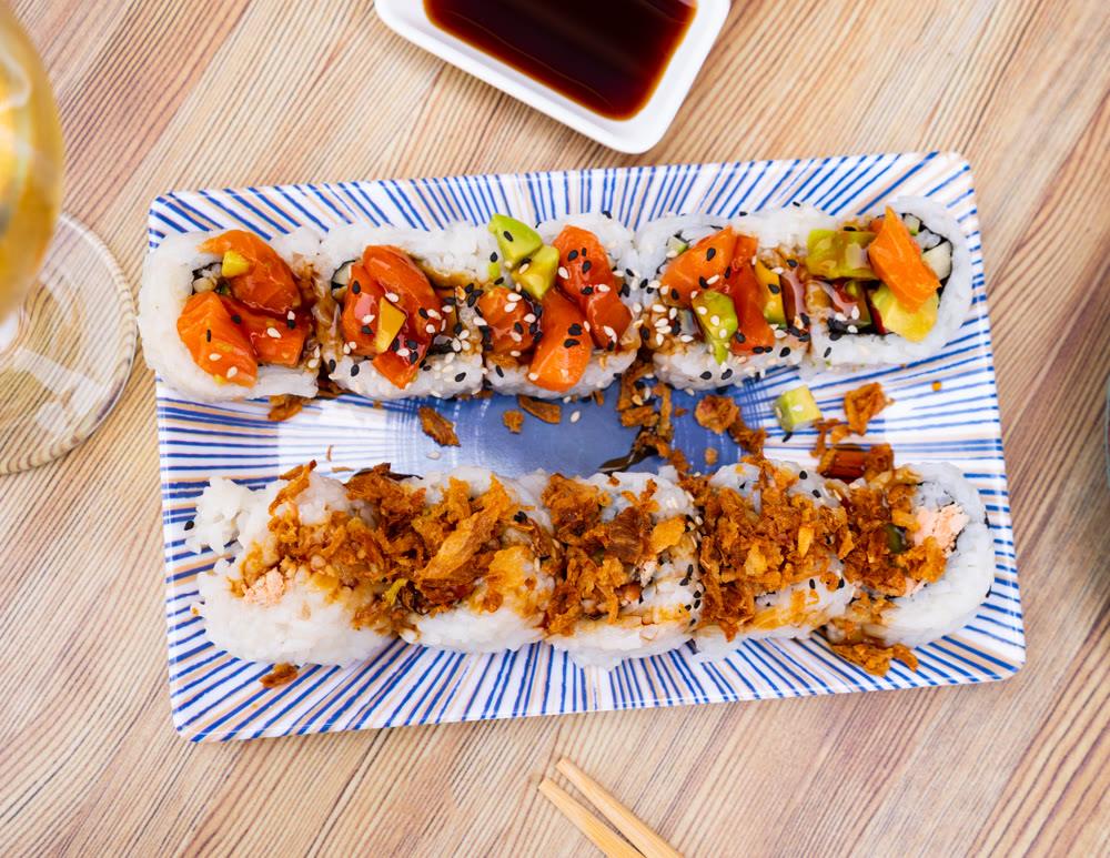 On table there is plate with set of sushi - uramaki rolls with cucumber, avocado crab and salmon