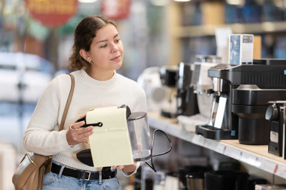 Positive girl choosing coffee machine in hypermarket