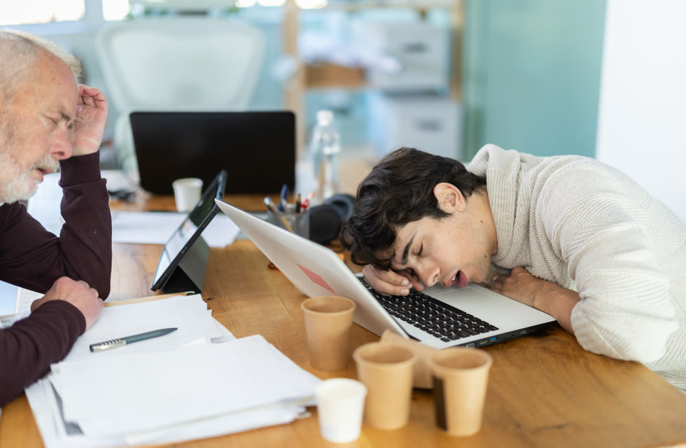 Wearied senior man and guy colleagues are dozing near workplace in office