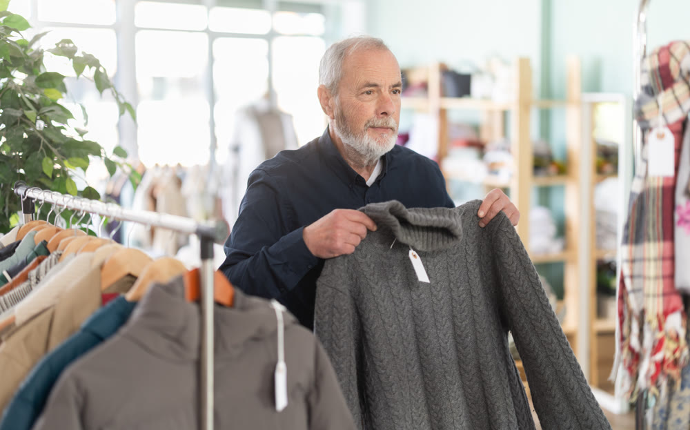 Elderly male shopper chooses fashionable sweater in clothing store
