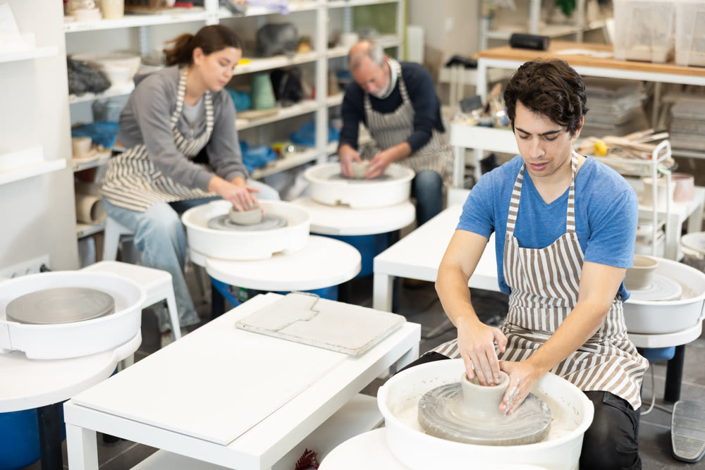 Young man shaping pottery on wheel in ceramics studio