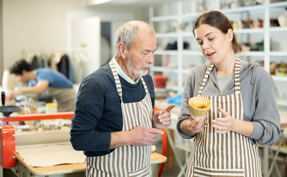 Young woman showing ceramic piece to elderly man
