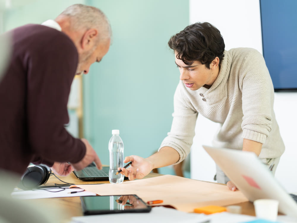 Young and elderly men colleagues discussing building plan in office