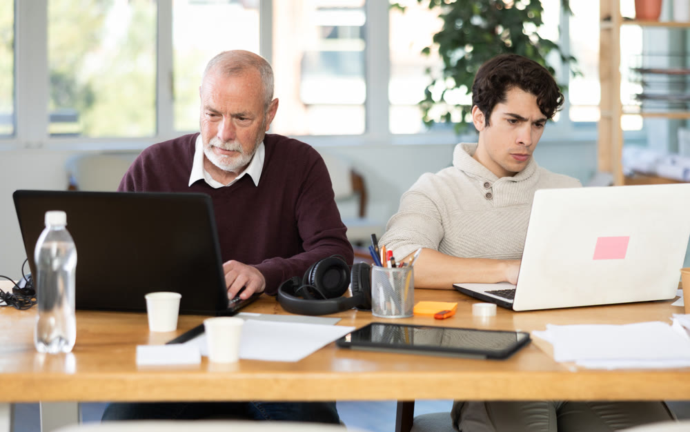 Two male manager work on laptops in modern company office