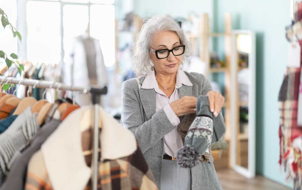 Mature woman in glasses chooses fashionable warm hat in clothing store