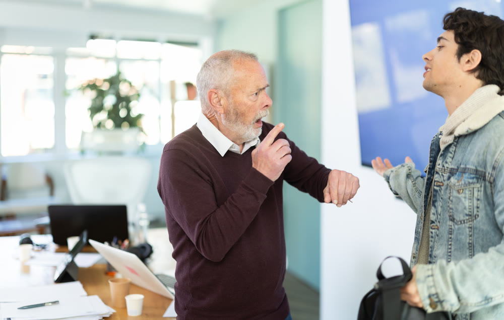 Elderly man scolding young male colleague for being late to office