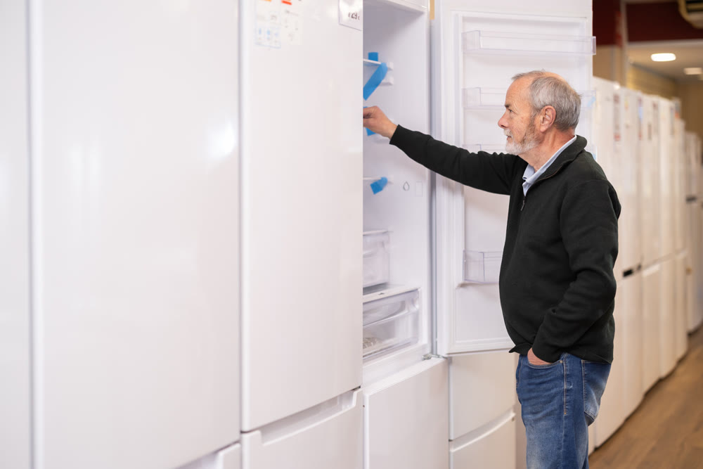 Elderly man chooses refrigerator in appliance store