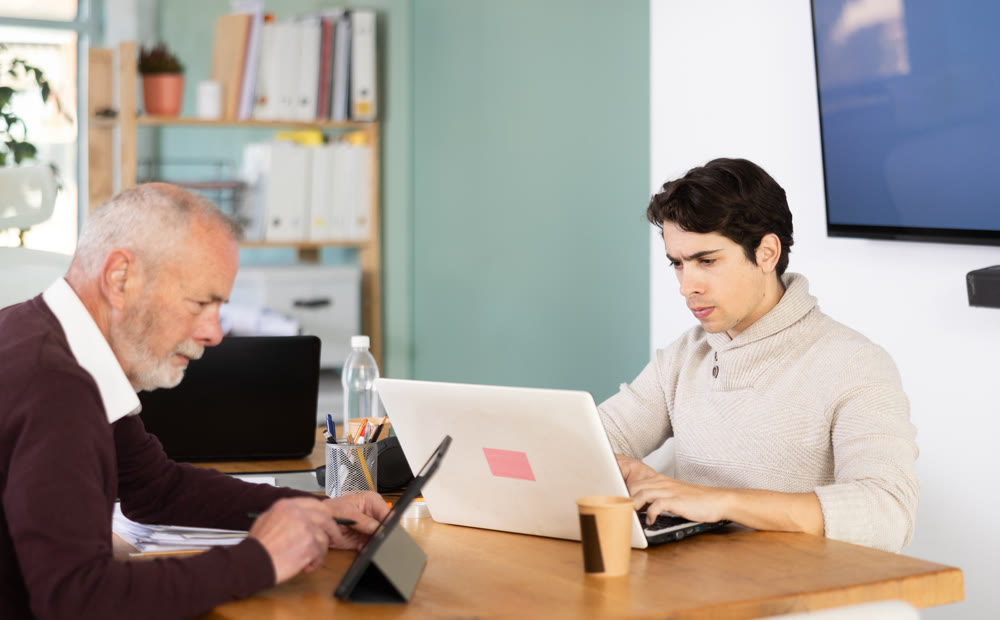 Two male manager work on laptops in modern company office