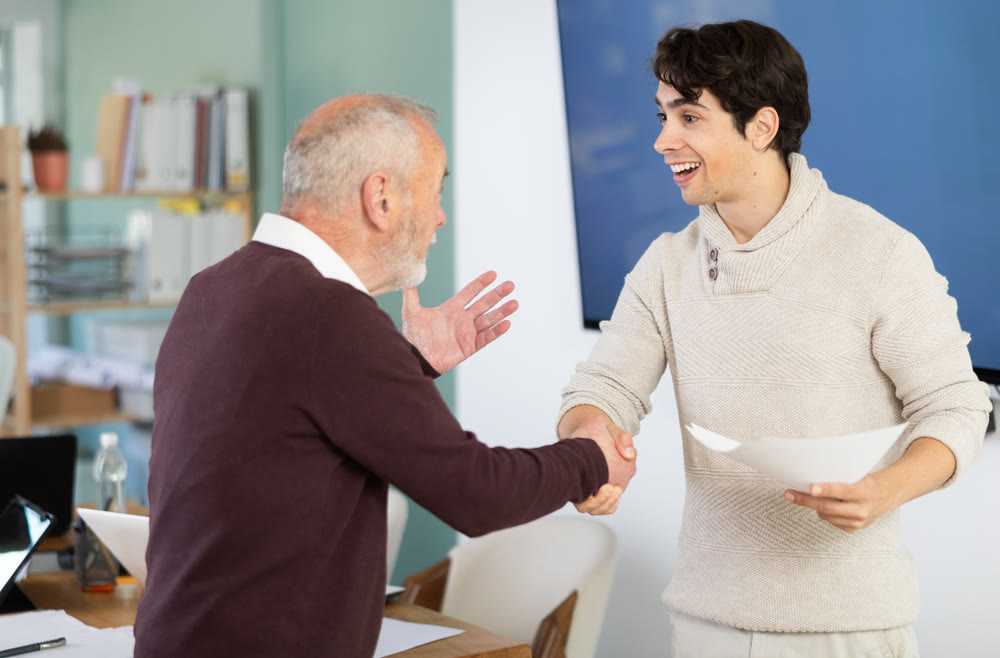 Young and elderly men shaking hands with documents in office