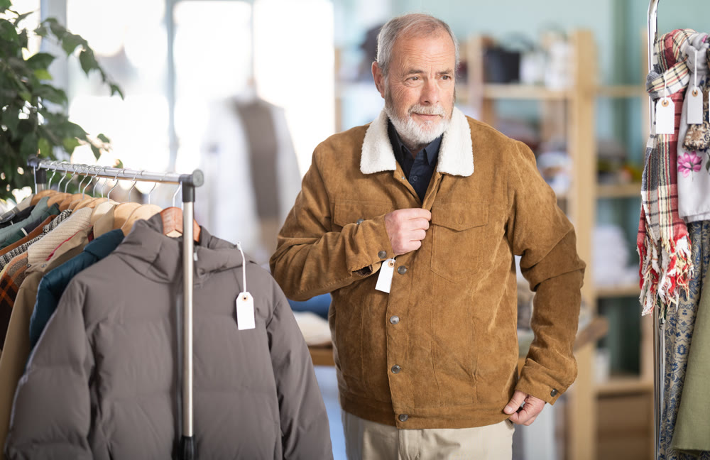 Elderly man trying on brown jacket in store