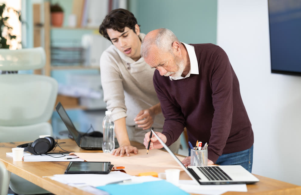Young and elderly men colleagues discussing building plan in office