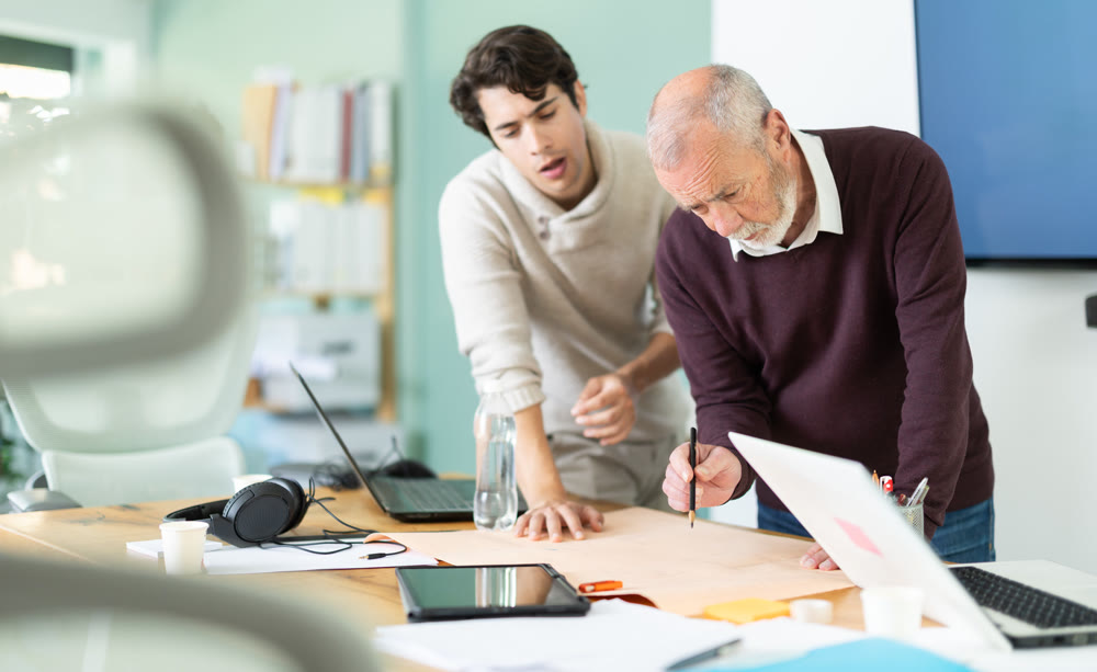 Young and elderly men colleagues discussing building plan in office