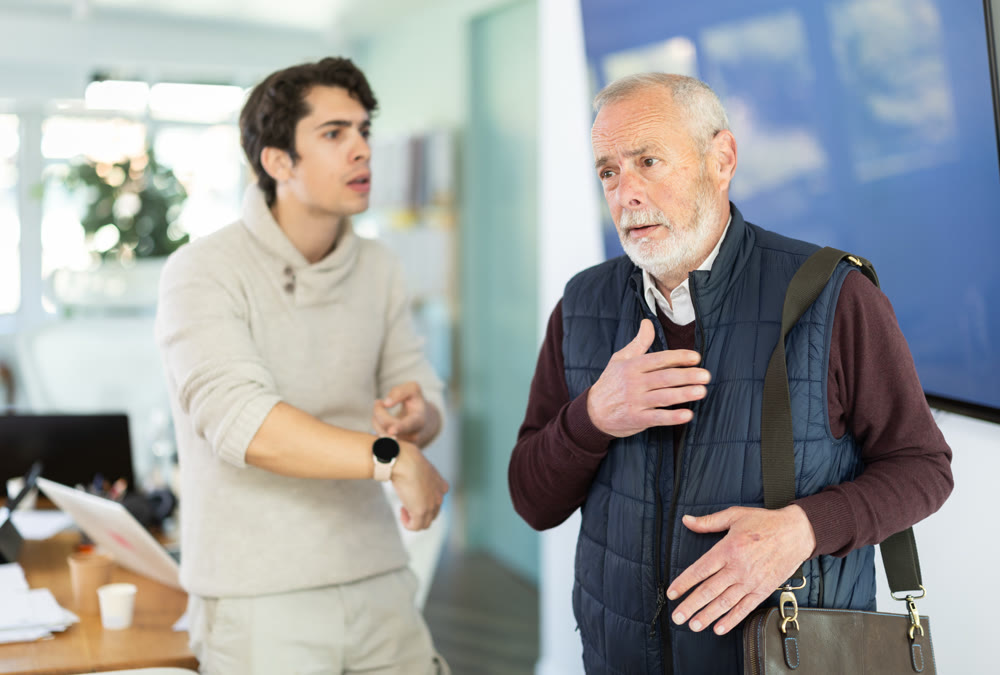 Young man scolding elderly male colleague for being late to office
