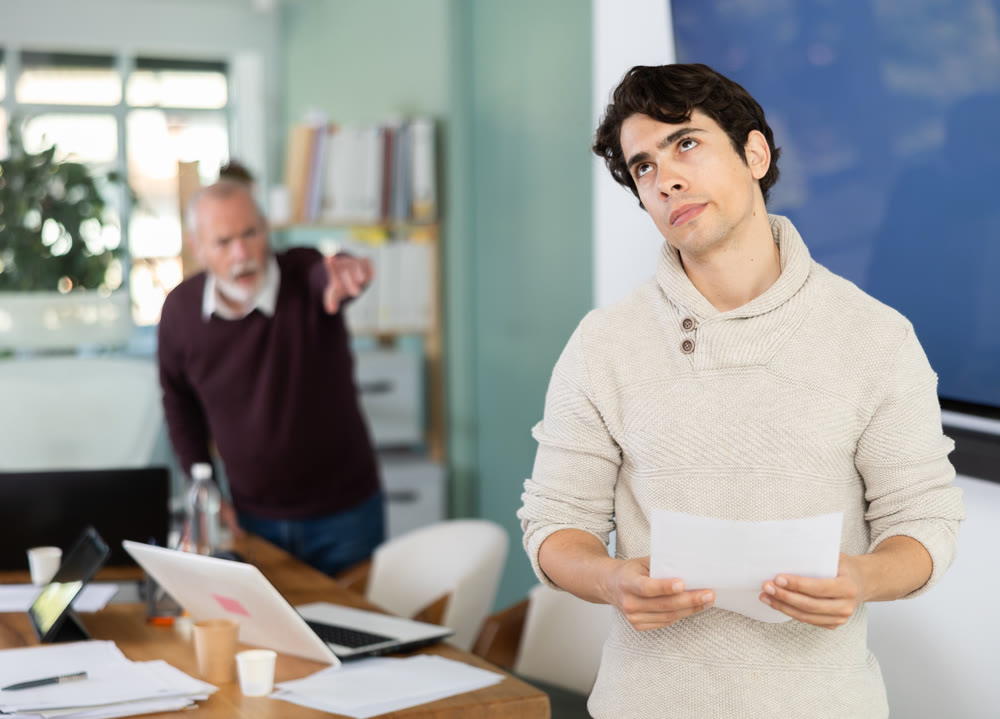 Elderly manager shows door to young employee who is holding resignation letter