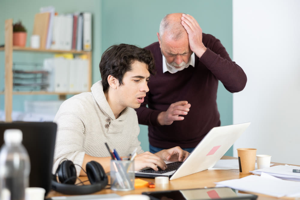 Sad young and elderly men facing problems while working on laptop