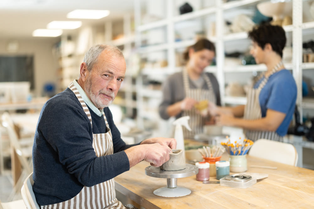 Mature man at table molds cup from wet clay in pottery workshop