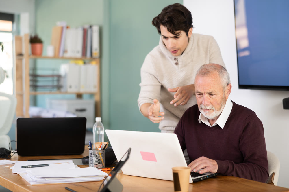 Guy helps elderly man complete task on laptop