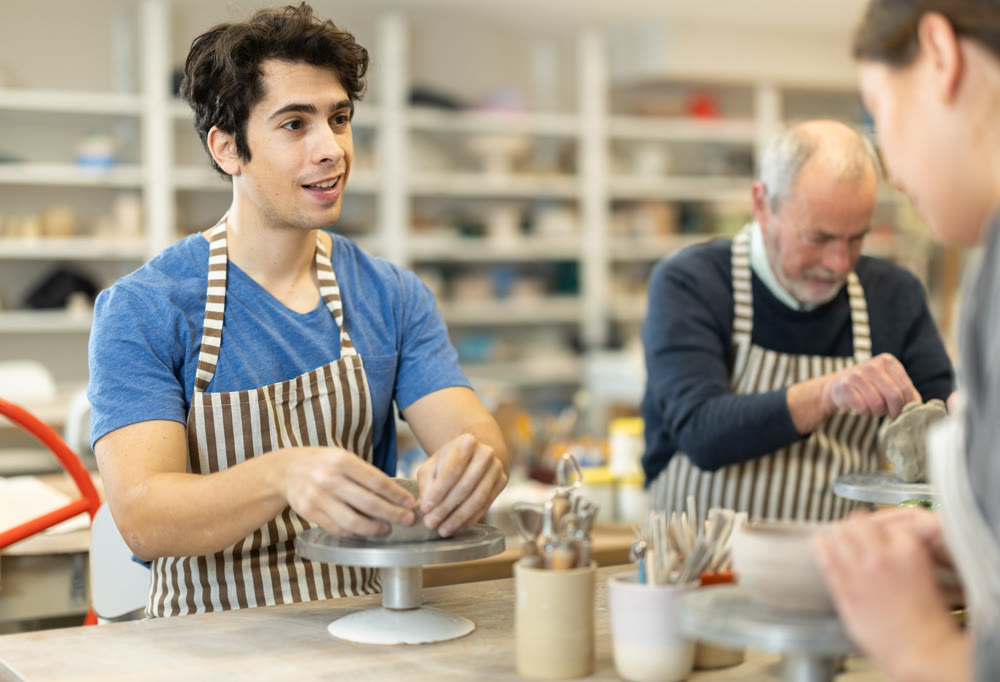 Man at table molds cup from wet clay in pottery workshop