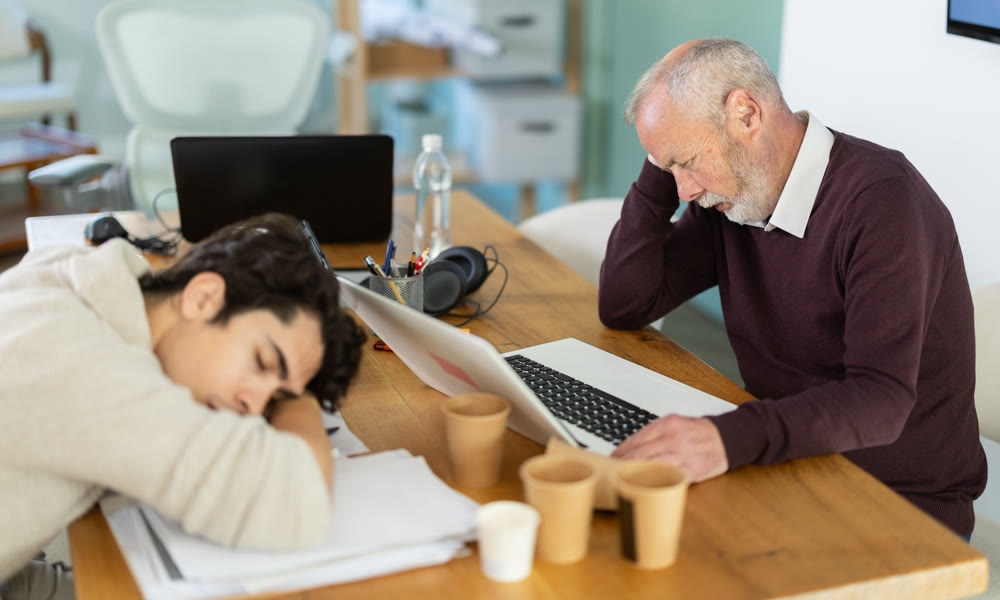 Wearied senior man and guy colleagues are dozing near workplace in office