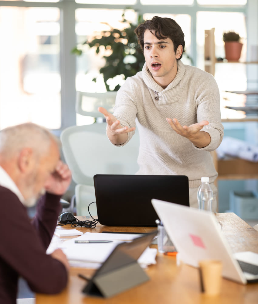 Young man scolding elderly man working on tablet in office