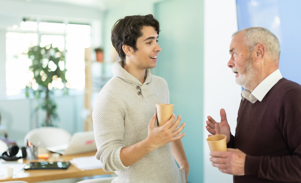 Young and elderly men colleagues drinking coffee in office