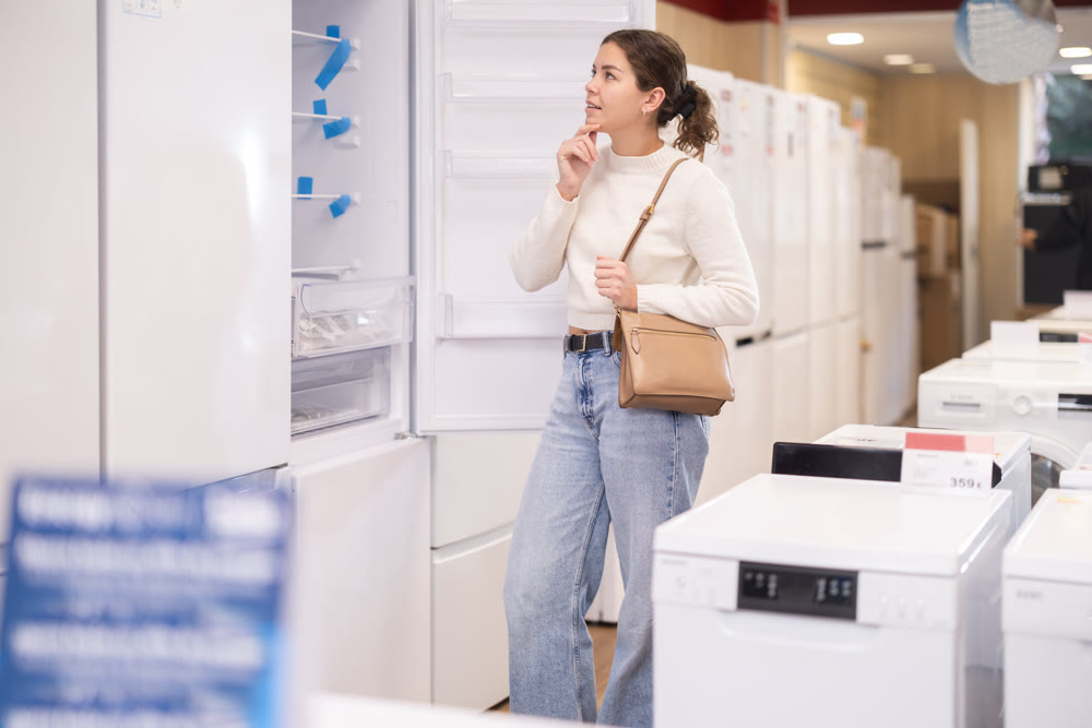 Young woman buyer examine fridge in detail before buying