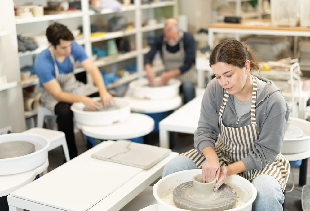 Young woman shaping pottery on wheel in ceramics studio