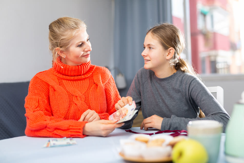 Mom gives pocket money to daughter. Joyful daughter thanks mom