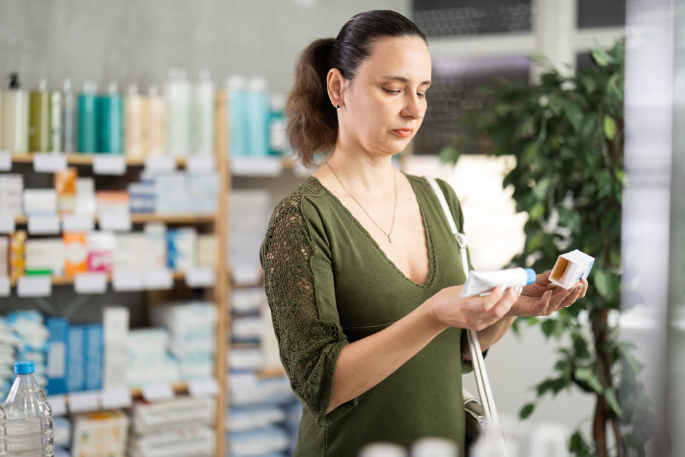 Middle-aged woman customer choosing ointment in box in drugstore