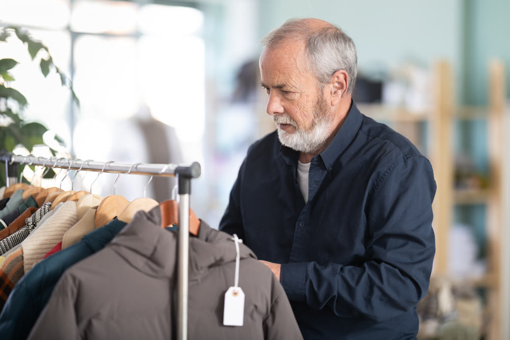 Elderly man chooses tries fashionable coat in clothing store