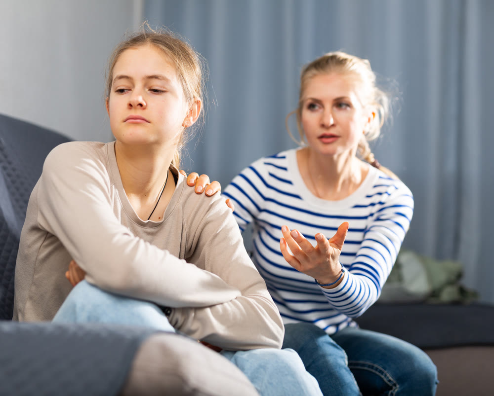 Sad female and daughter sitting at sofa and having quarrel
