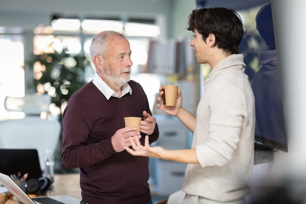 Young and elderly men colleagues drinking coffee in office