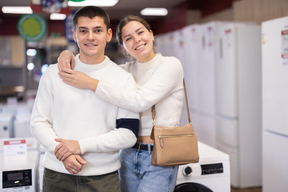 Young couple chooses modern washing machine or dishwasher at hypermarket