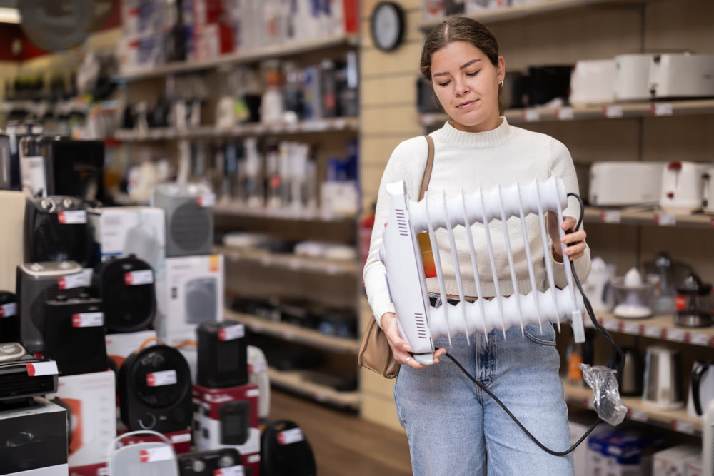 Young woman chooses oil heater in appliance store