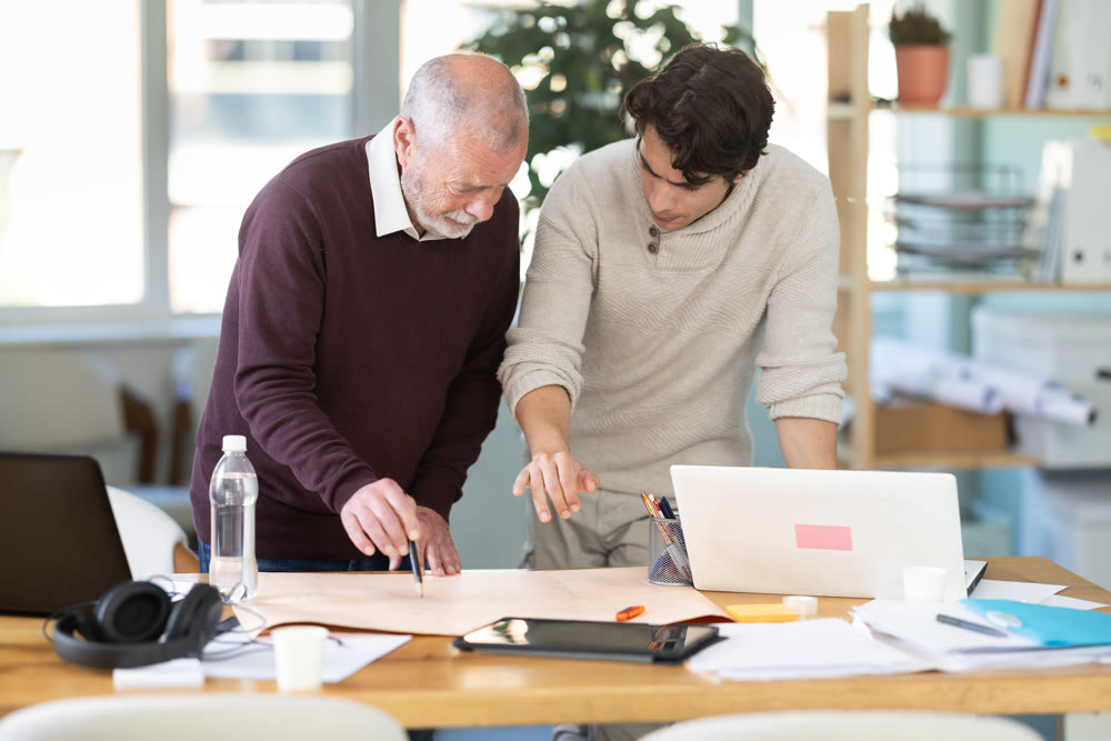 Young and elderly men colleagues discussing building plan in office