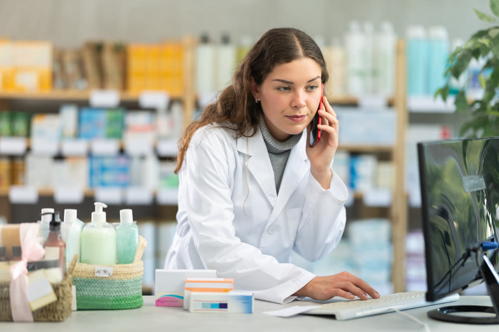 Female pharmacist working at computer and talking on phone